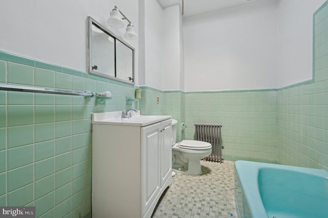 bathroom with vanity, radiator, toilet, tile walls, and a tub