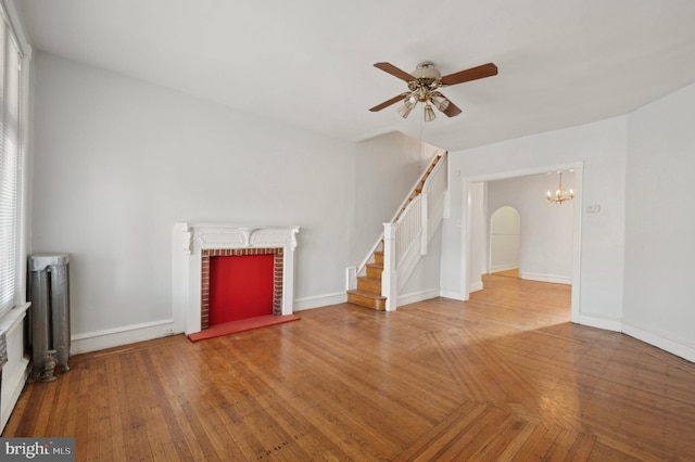 unfurnished living room with hardwood / wood-style flooring, ceiling fan with notable chandelier, and radiator