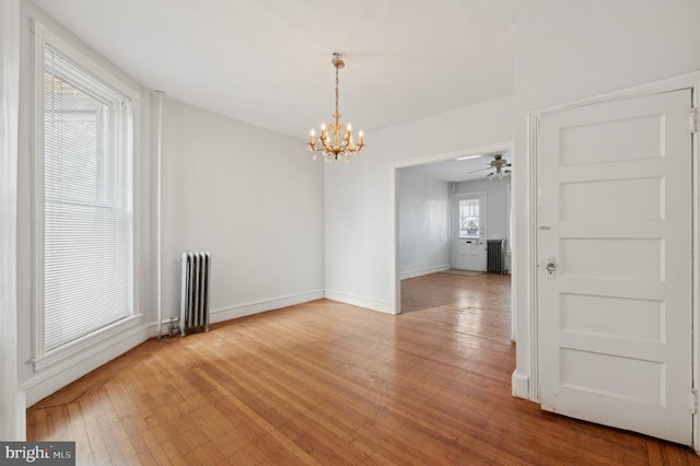 unfurnished dining area with radiator, ceiling fan with notable chandelier, and light wood-type flooring