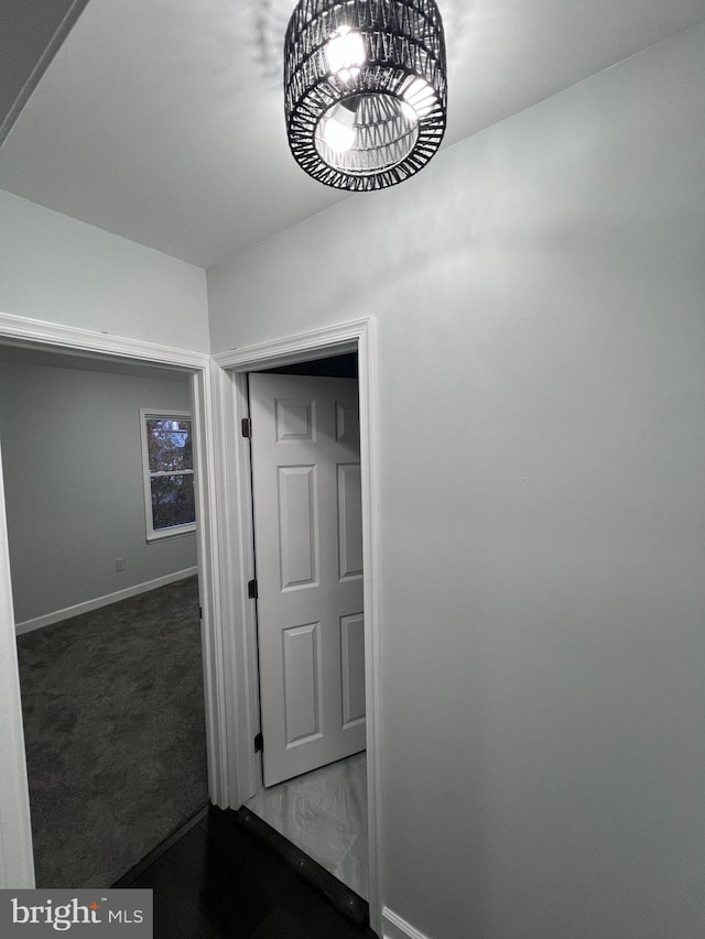 hallway with a notable chandelier and dark carpet