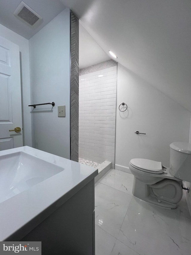 bathroom with a tile shower, vanity, vaulted ceiling, and toilet