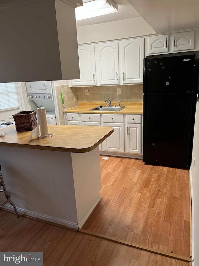 kitchen with decorative backsplash, white cabinetry, black refrigerator, and sink