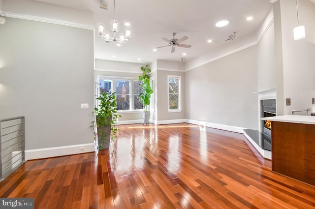 unfurnished living room featuring hardwood / wood-style floors, ceiling fan with notable chandelier, and crown molding