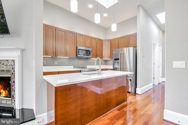 kitchen featuring appliances with stainless steel finishes, light wood-type flooring, sink, a tile fireplace, and pendant lighting