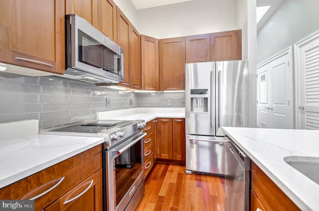 kitchen featuring tasteful backsplash, light stone counters, stainless steel appliances, and light wood-type flooring