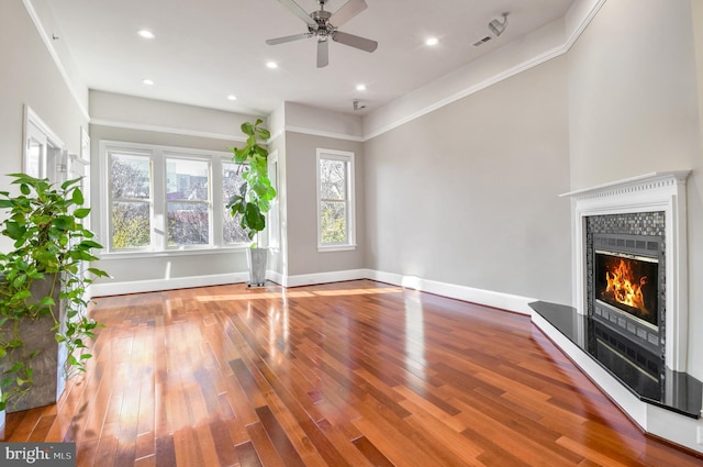 unfurnished living room featuring hardwood / wood-style flooring, ceiling fan, ornamental molding, and a tile fireplace