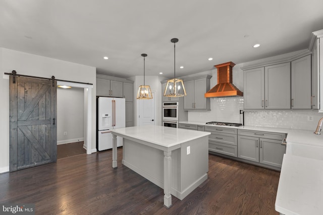 kitchen with a barn door, dark hardwood / wood-style flooring, gray cabinets, custom range hood, and appliances with stainless steel finishes