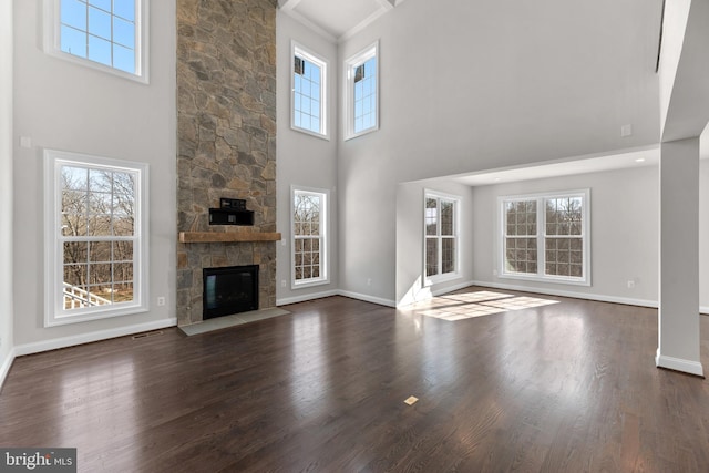 unfurnished living room featuring dark hardwood / wood-style flooring, plenty of natural light, a towering ceiling, and a stone fireplace