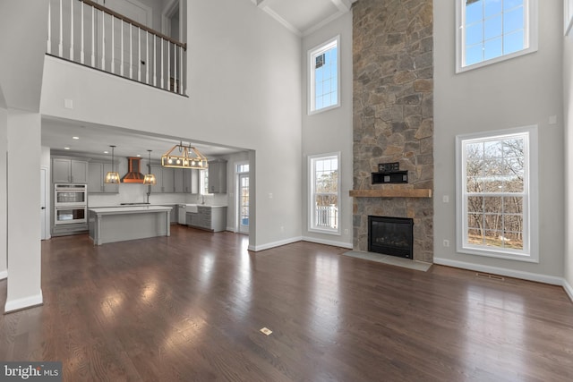 unfurnished living room with sink, dark wood-type flooring, a stone fireplace, a towering ceiling, and ornamental molding