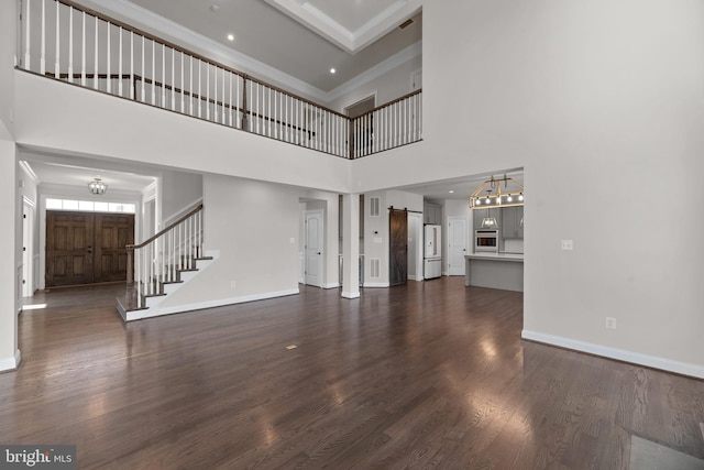 unfurnished living room featuring a high ceiling, a barn door, and dark hardwood / wood-style floors