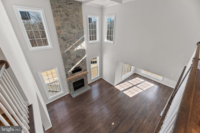 unfurnished living room with a stone fireplace, dark hardwood / wood-style flooring, a high ceiling, and ornamental molding