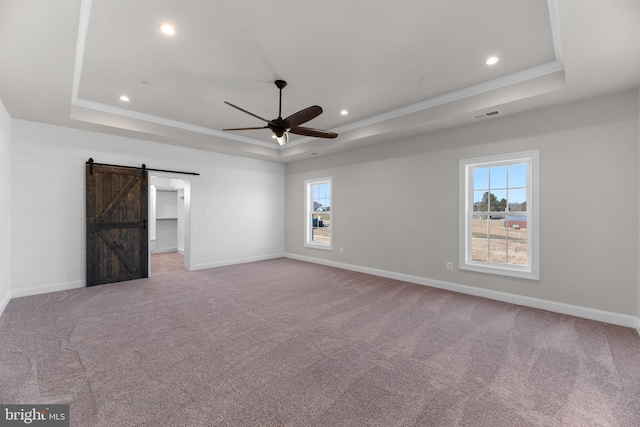 empty room with a barn door, light colored carpet, a raised ceiling, and crown molding