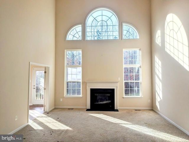 unfurnished living room featuring a wealth of natural light, a towering ceiling, and light carpet