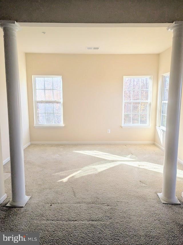 spare room featuring ornate columns and light carpet