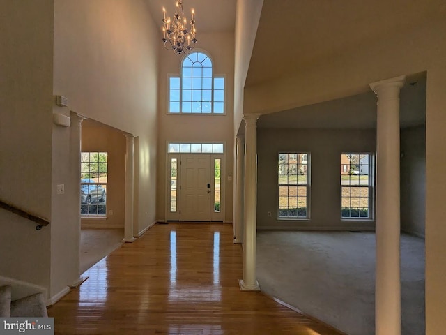 carpeted foyer featuring a notable chandelier, a high ceiling, and decorative columns