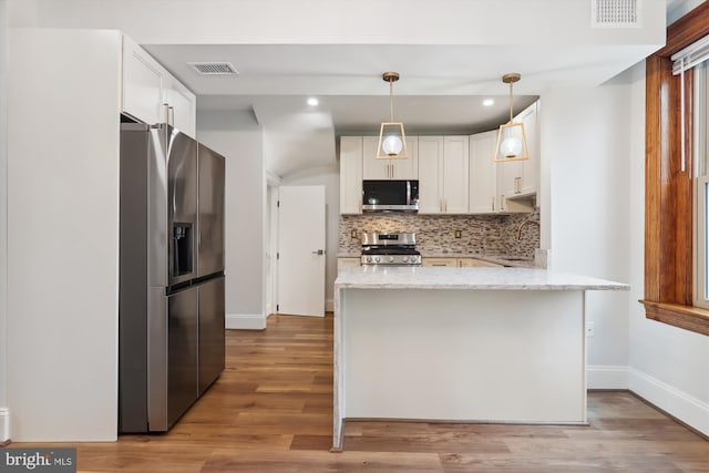 kitchen featuring stainless steel appliances, white cabinetry, hanging light fixtures, and light hardwood / wood-style flooring