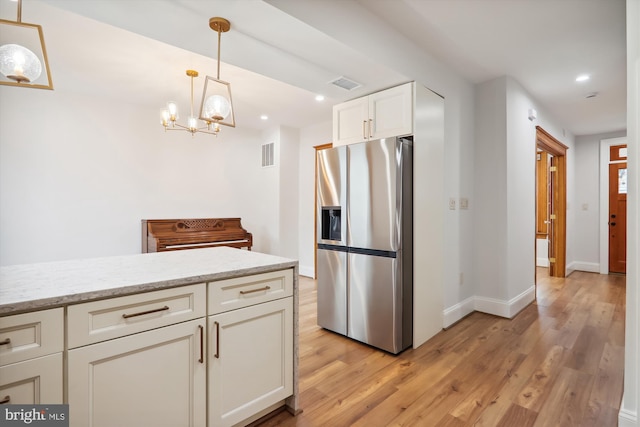 kitchen with light stone counters, light hardwood / wood-style flooring, stainless steel refrigerator with ice dispenser, and a notable chandelier