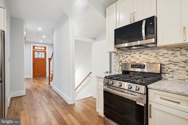 kitchen with tasteful backsplash, light stone counters, light hardwood / wood-style flooring, white cabinets, and appliances with stainless steel finishes