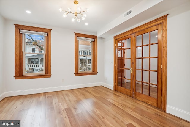 spare room featuring a notable chandelier, light hardwood / wood-style floors, and french doors