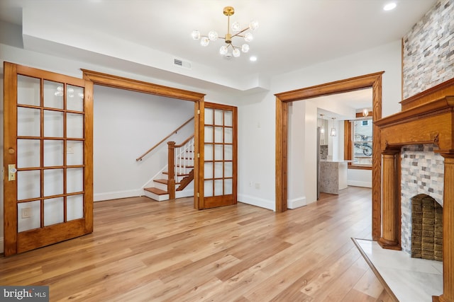 unfurnished living room featuring a large fireplace, an inviting chandelier, french doors, and light hardwood / wood-style flooring