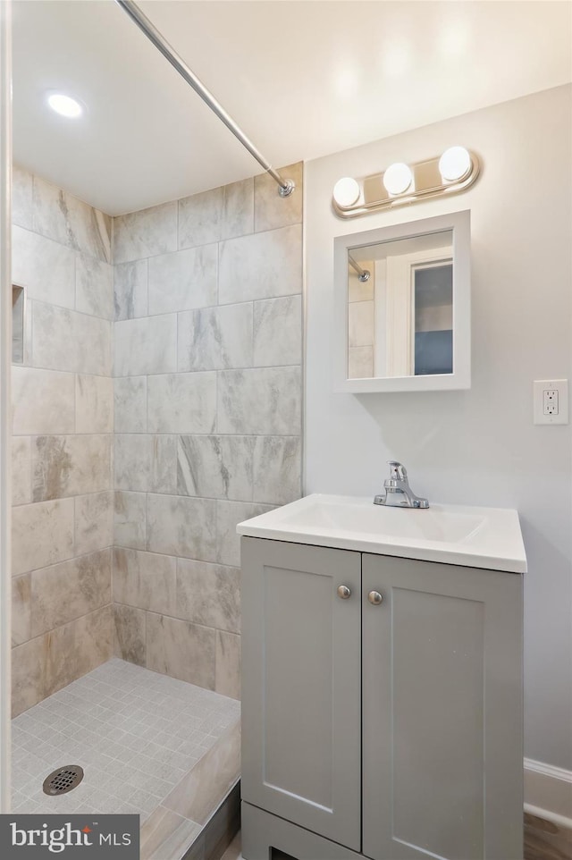 bathroom with a tile shower, vanity, and wood-type flooring