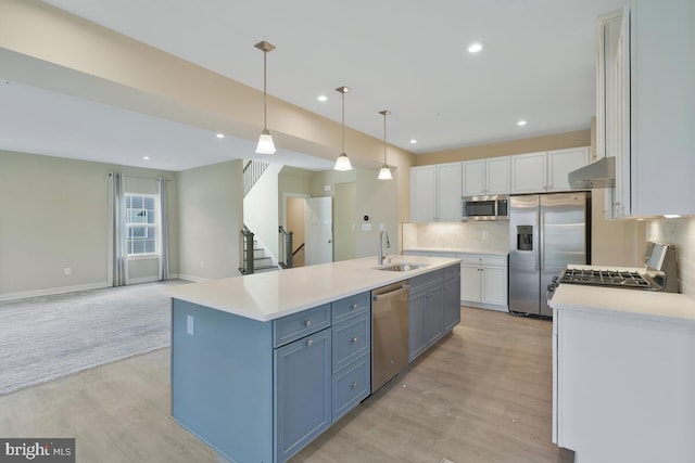 kitchen with white cabinets, a center island with sink, sink, appliances with stainless steel finishes, and decorative light fixtures