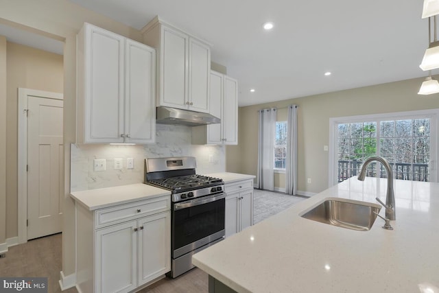 kitchen with light stone countertops, white cabinetry, sink, stainless steel gas range oven, and a kitchen island with sink