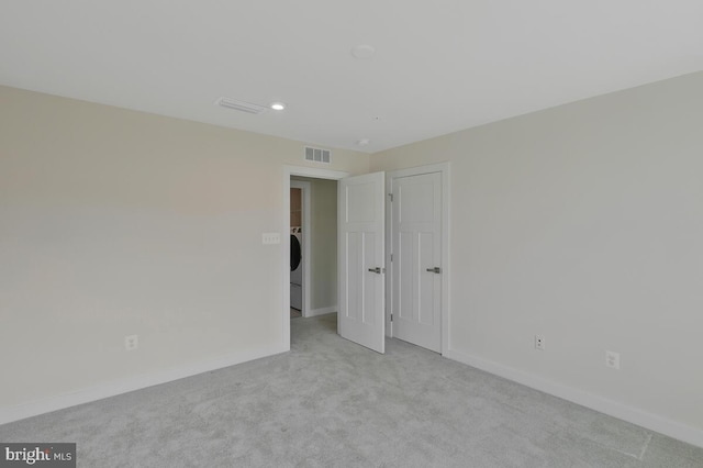 unfurnished bedroom with light colored carpet and washer / clothes dryer