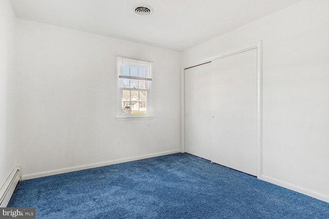 unfurnished bedroom featuring dark colored carpet, baseboard heating, and a closet