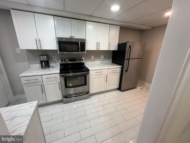 kitchen featuring a paneled ceiling, white cabinets, light tile patterned flooring, and appliances with stainless steel finishes