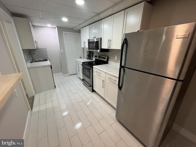 kitchen featuring appliances with stainless steel finishes, light stone counters, a drop ceiling, sink, and white cabinets