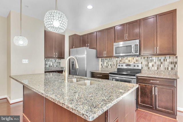 kitchen featuring decorative backsplash, appliances with stainless steel finishes, light stone counters, pendant lighting, and light hardwood / wood-style flooring