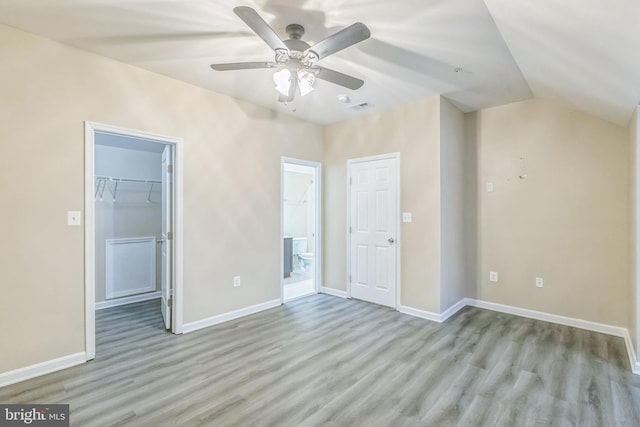 unfurnished bedroom with ensuite bathroom, a walk in closet, light hardwood / wood-style flooring, ceiling fan, and a closet