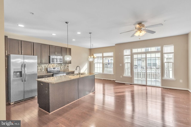 kitchen featuring dark hardwood / wood-style floors, light stone countertops, an island with sink, appliances with stainless steel finishes, and dark brown cabinets