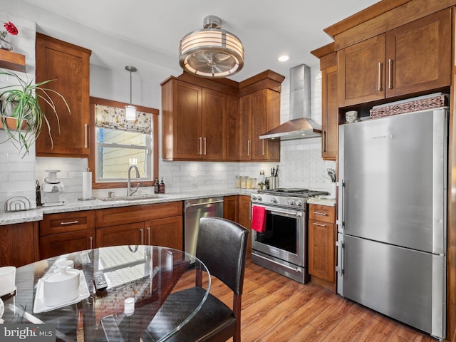 kitchen featuring wall chimney range hood, sink, light hardwood / wood-style floors, light stone counters, and stainless steel appliances