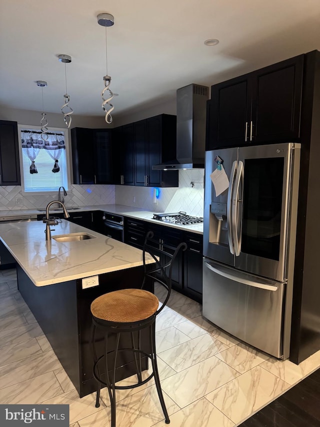 kitchen with wall chimney range hood, gas stovetop, stainless steel fridge, pendant lighting, and a kitchen bar