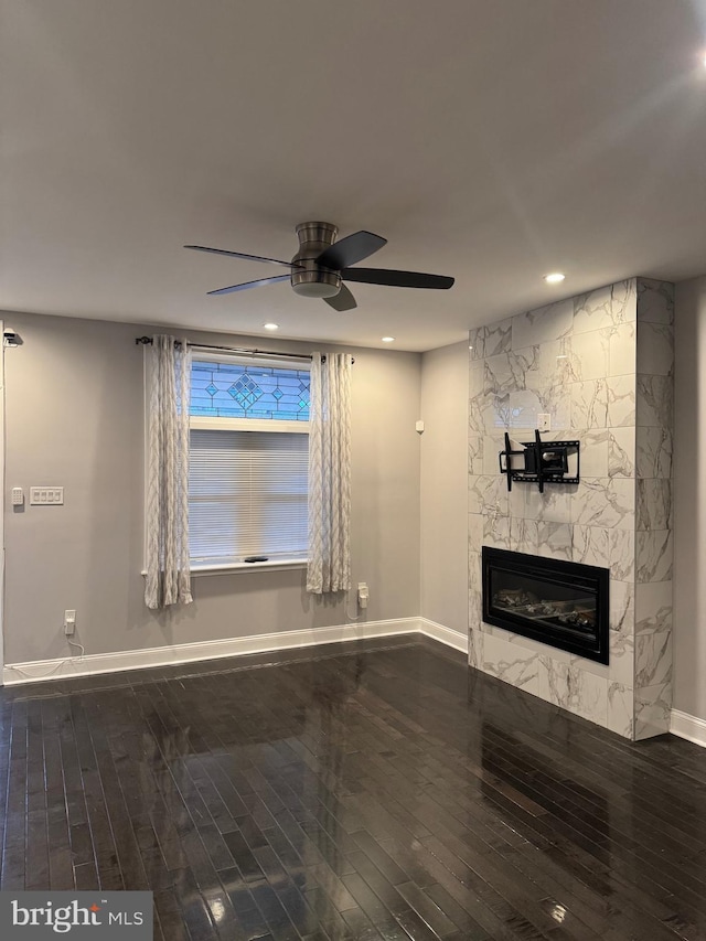 unfurnished living room with a stone fireplace, ceiling fan, and dark wood-type flooring