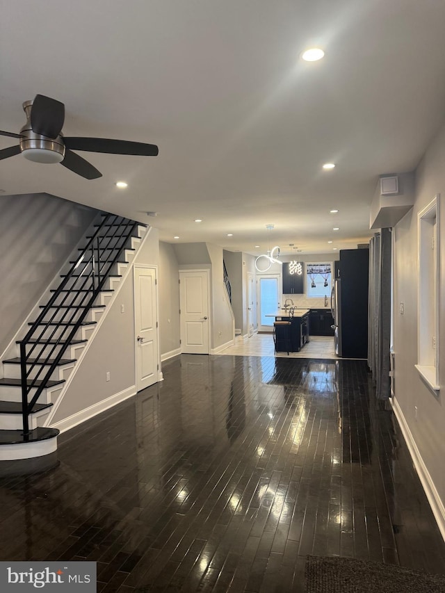 unfurnished living room with ceiling fan, sink, and dark wood-type flooring