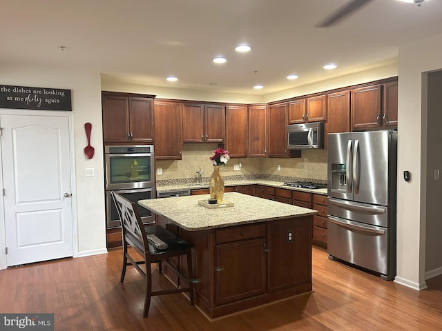 kitchen featuring dark wood finished floors, decorative backsplash, a kitchen island, appliances with stainless steel finishes, and light stone countertops