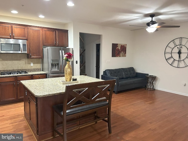 kitchen with decorative backsplash, light stone countertops, stainless steel appliances, light wood-type flooring, and a kitchen bar