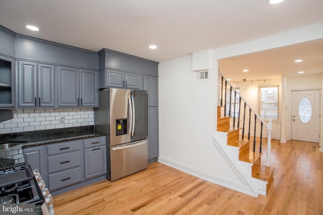 kitchen featuring stainless steel fridge, tasteful backsplash, dark stone countertops, and light hardwood / wood-style flooring