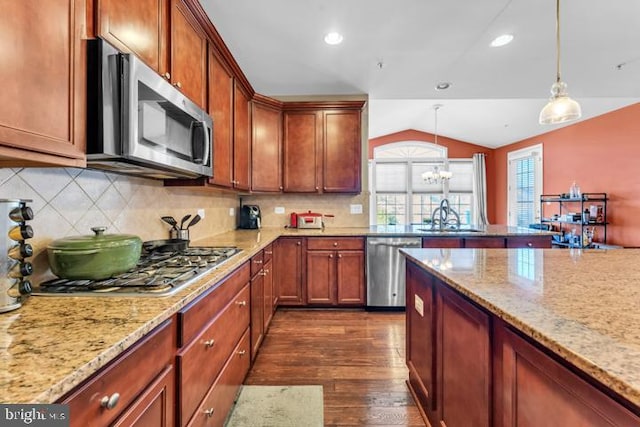 kitchen with appliances with stainless steel finishes, vaulted ceiling, sink, dark hardwood / wood-style floors, and hanging light fixtures