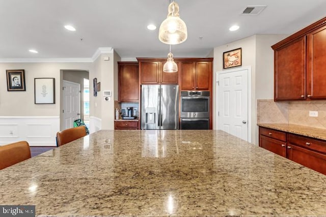 kitchen featuring light stone countertops, hanging light fixtures, crown molding, a kitchen bar, and appliances with stainless steel finishes