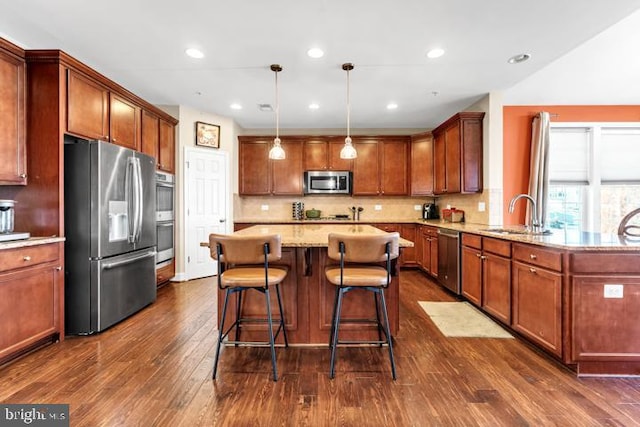 kitchen featuring light stone counters, stainless steel appliances, dark wood-type flooring, sink, and pendant lighting