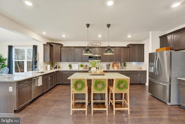 kitchen featuring a kitchen bar, appliances with stainless steel finishes, decorative light fixtures, and dark wood-type flooring