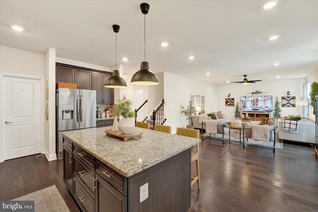 kitchen featuring dark wood-type flooring, ceiling fan, dark brown cabinetry, a kitchen bar, and stainless steel fridge with ice dispenser