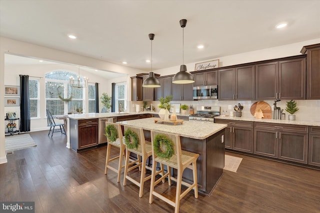 kitchen with a center island, stainless steel appliances, hanging light fixtures, and tasteful backsplash