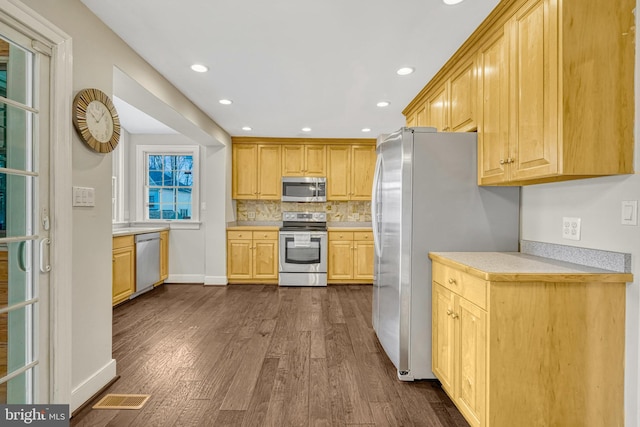 kitchen with tasteful backsplash, light brown cabinetry, dark hardwood / wood-style flooring, and appliances with stainless steel finishes