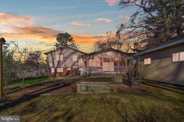 back house at dusk featuring a lawn and a sunroom