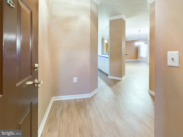 corridor with light hardwood / wood-style floors, crown molding, and a notable chandelier